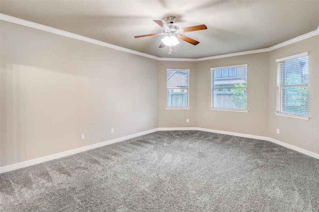 Retreat in comfort to the spacious first-floor primary suite, complete with soft carpet underfoot, crown molding above, and a wall of windows that fills the room with natural light.
