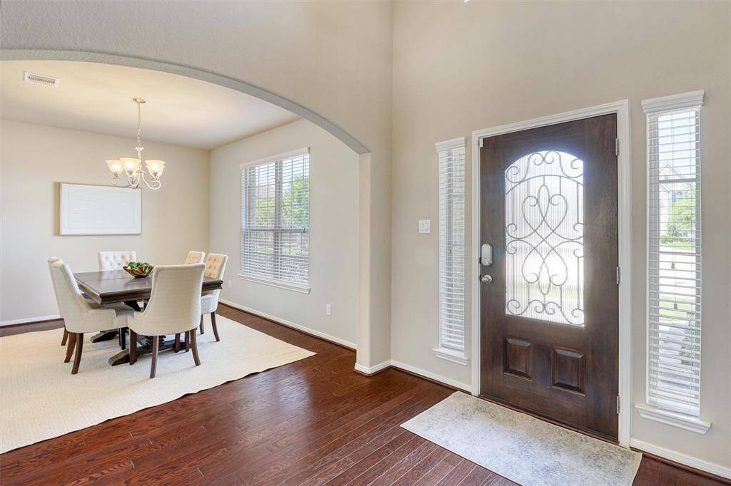 Step into a warm welcome with this stunning foyer featuring rich engineered wood flooring, soaring ceilings, and a decorative front door flanked by tall transom windows—setting the tone for timeless elegance throughout.