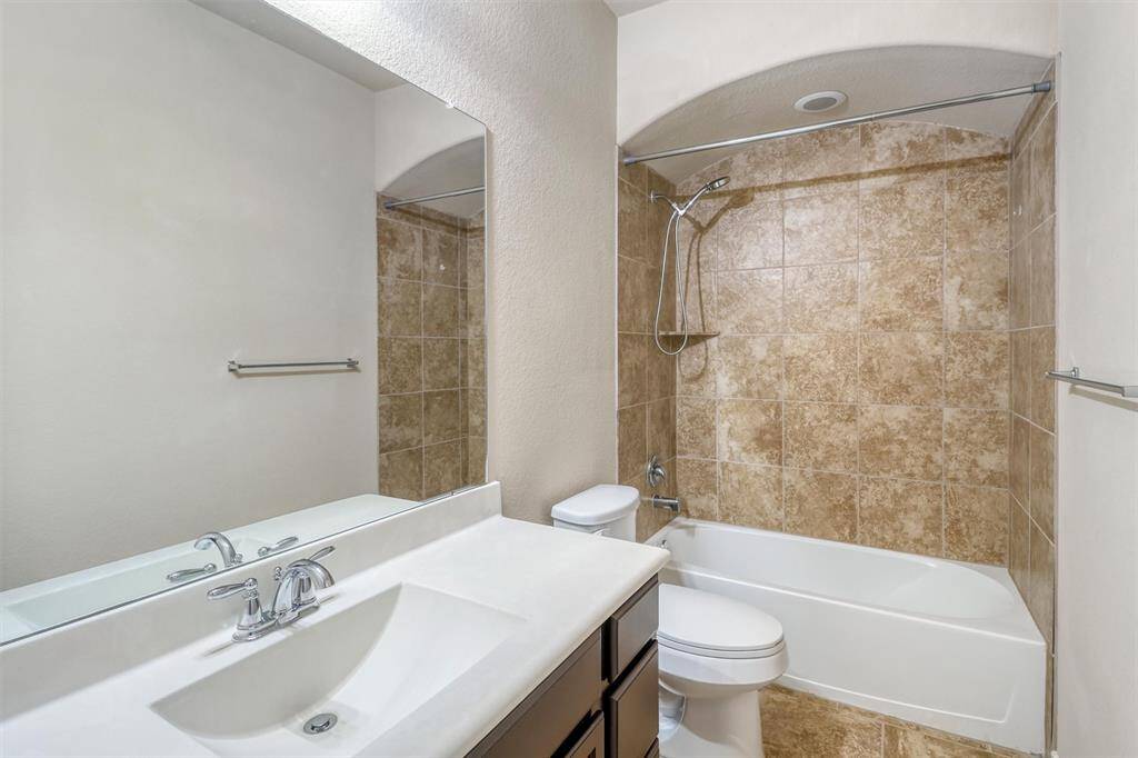 The private bath includes a sleek single-sink vanity, designer tile flooring, and a fully tiled tub/shower enclosure with an arched inset and updated fixtures.