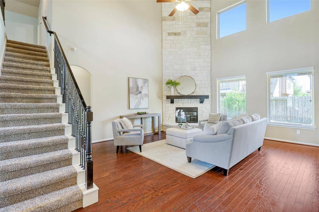 A grand staircase and soaring ceilings frame the spacious family room, where rich hardwood floors and a striking floor-to-ceiling stone fireplace create an inviting and elegant retreat.