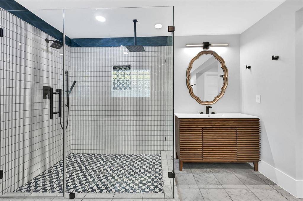 Experience the elegance of this large walk-in shower featuring double shower heads, custom tile work, and a modern vanity with sleek black accents for a stylish and functional bathroom retreat.