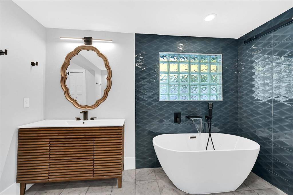 Indulge in the luxury of this soaking tub, complete with a wall-mounted waterfall faucet, custom wall tile, and a modern vanity with bold black accents, creating a serene and sophisticated bathroom retreat.