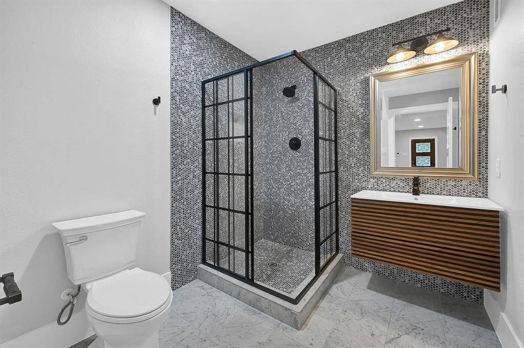 This sleek bathroom boasts a modern walk-in shower with custom tile work, stylish black accents, a contemporary wall-mounted vanity, and elegant tile flooring, creating a spa-like atmosphere for ultimate relaxation.