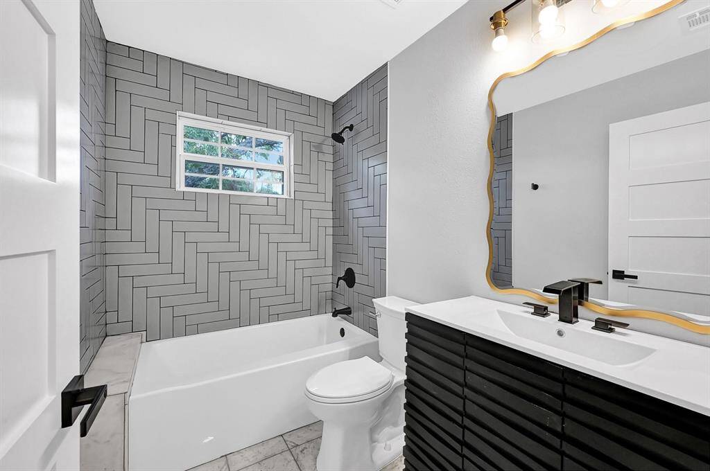 This stylish bathroom features a shower/tub combo with custom grey tiles, a sleek black vanity with matching black accents, and a modern toilet, offering both functionality and contemporary design.