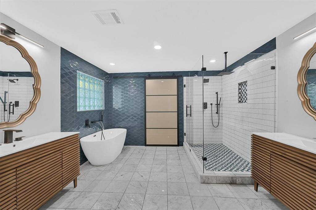 The primary bathroom offers a luxurious open design with a large walk-in shower, a standalone bathtub, sleek tile flooring, and recessed lighting, creating a spa-like retreat.