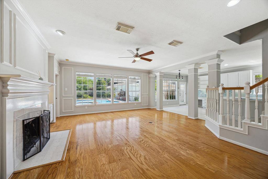 Brimming with natural light and timeless charm, this spacious family room features rich hardwood floors, elegant molding, custom built-ins with sconce lighting, and a romantic gas fireplace with a detailed mantle. A wall of windows offers serene views of the sparkling pool, creating a warm and welcoming space for everyday living or entertaining.