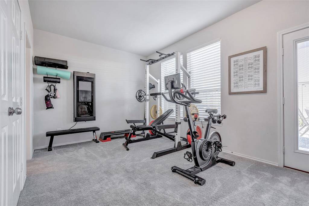This room is currently set up as a home gym with various exercise equipment, featuring ample space, neutral decor, and good natural light from the window.