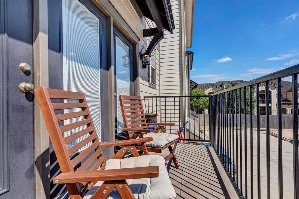 This photo showcases a cozy balcony with two wooden chairs and cushions, enclosed by a metal railing. The space offers an inviting area for relaxation with a view of the surrounding neighborhood.