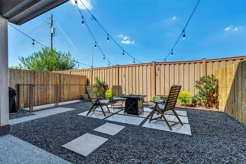 This is a cozy, low-maintenance backyard with modern gravel landscaping, featuring a seating area with a table and chairs, and strung outdoor lights for ambiance. It's enclosed by a tall wooden privacy fence.