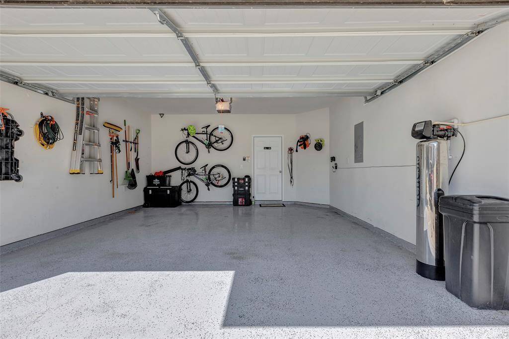 This is a clean, spacious two-car garage with an organized storage system on the walls, a speckled epoxy-coated floor for durability, and a water softener unit. It also features an access door to the interior of the home.