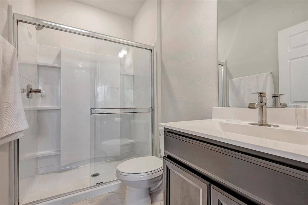 This is a modern bathroom featuring a glass-enclosed shower, a sleek vanity with ample counter space, and crisp white walls that contribute to a bright and clean aesthetic.