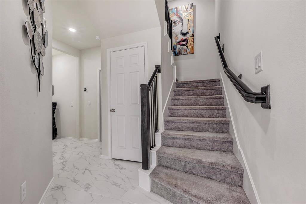 This is a modern entryway featuring marble tile flooring, a carpeted staircase with a wooden banister, and neutral wall colors accented by a bold artwork and a decorative wall piece.