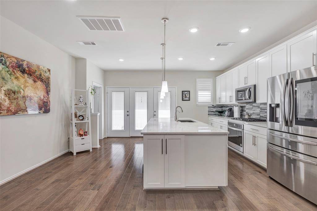 Modern kitchen with stainless steel appliances, white cabinetry, an island, and hardwood flooring. Bright, open space with recessed lighting. The kitchen is attached to a balcony perfect open concept for entertaining.