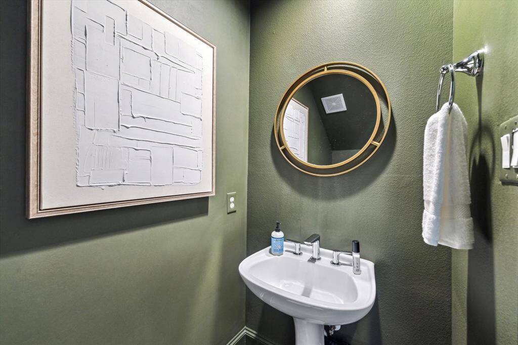 This stylish powder bath, conveniently located on the first floor, features a modern pedestal sink, sleek fixtures, and bold designer paint—perfect for guests and everyday use.