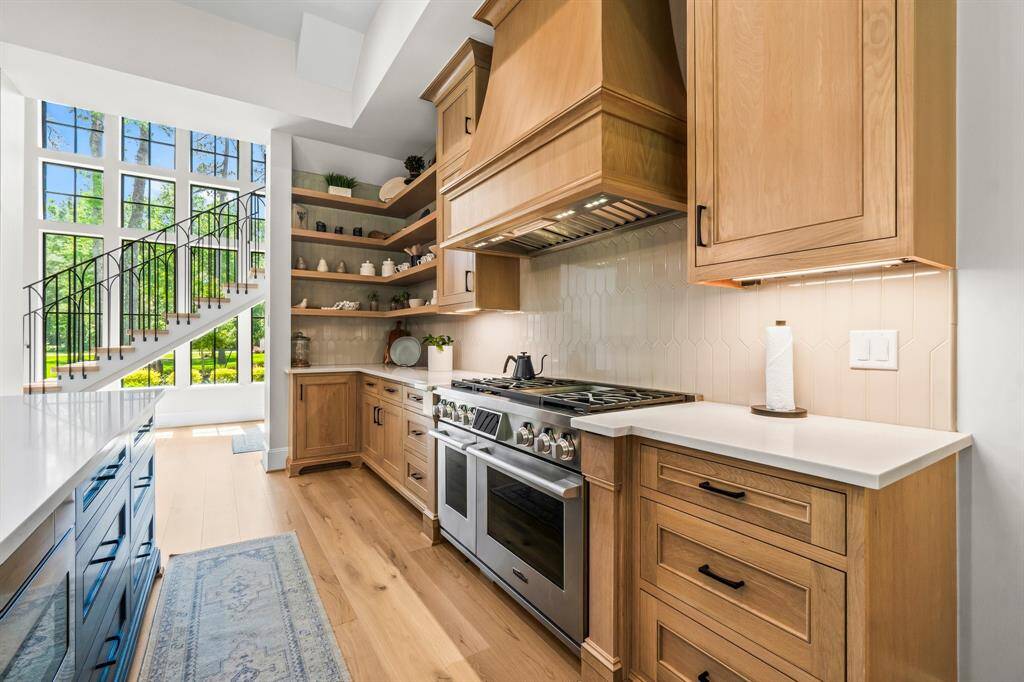 This photo showcases a spacious, open-concept kitchen with abundant natural light. It features a large island with seating, elegant pendant lighting, and light wood cabinetry.