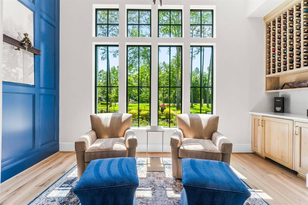 This bright wine room/ study features large windows that offer scenic views of the lush outdoors. It includes a stylish blue accent wall, hardwood floors, and a built-in wine rack, combining functionality with a touch of elegance.