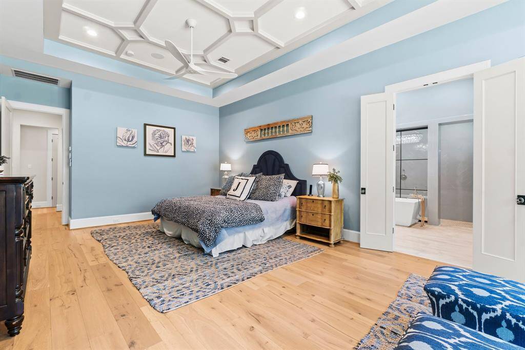 This spacious bedroom features an elegant tray ceiling and recessed lighting. It includes hardwood floors, and a stylish ensuite bathroom with a freestanding tub. The room is bright and inviting, perfect for relaxation.