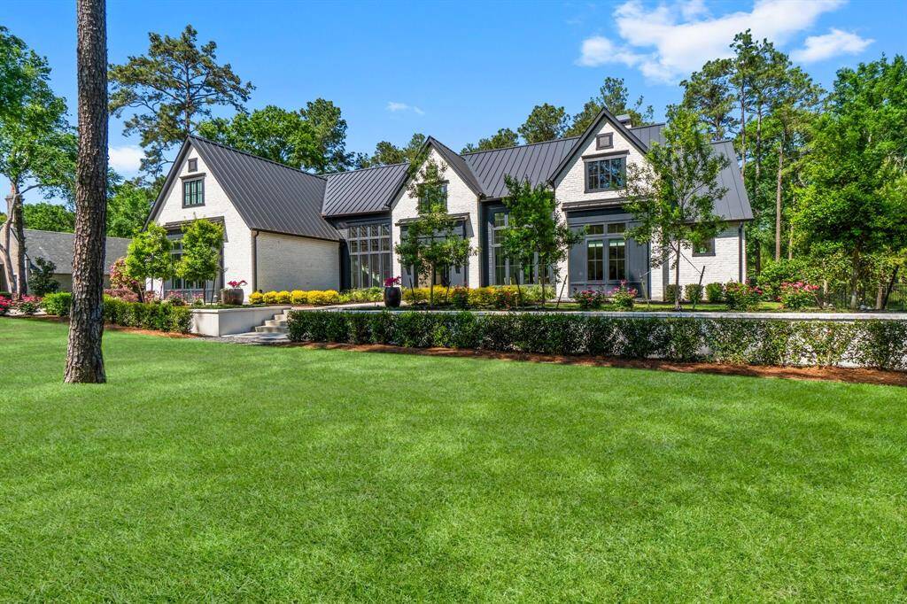 This photo highlights the modern farmhouse-style home with expansive windows and a well-manicured front yard framed by trees create a welcoming feel to the property.