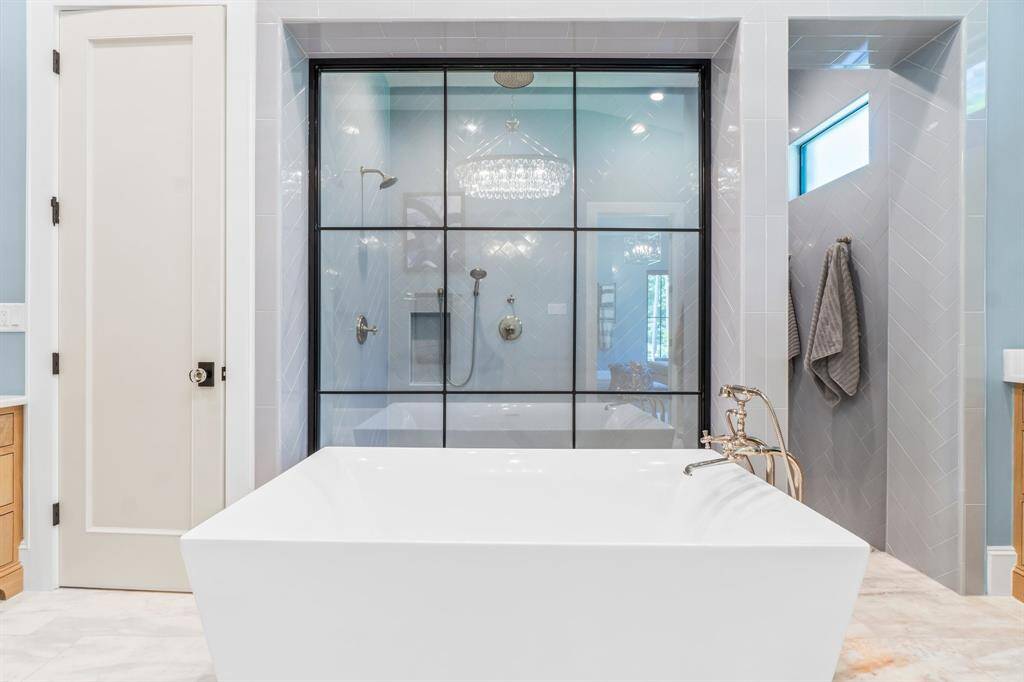 This photo showcases a modern bathroom featuring a sleek, freestanding bathtub with elegant fixtures. Behind it, is a spacious, glass-enclosed shower with high-end finishes.