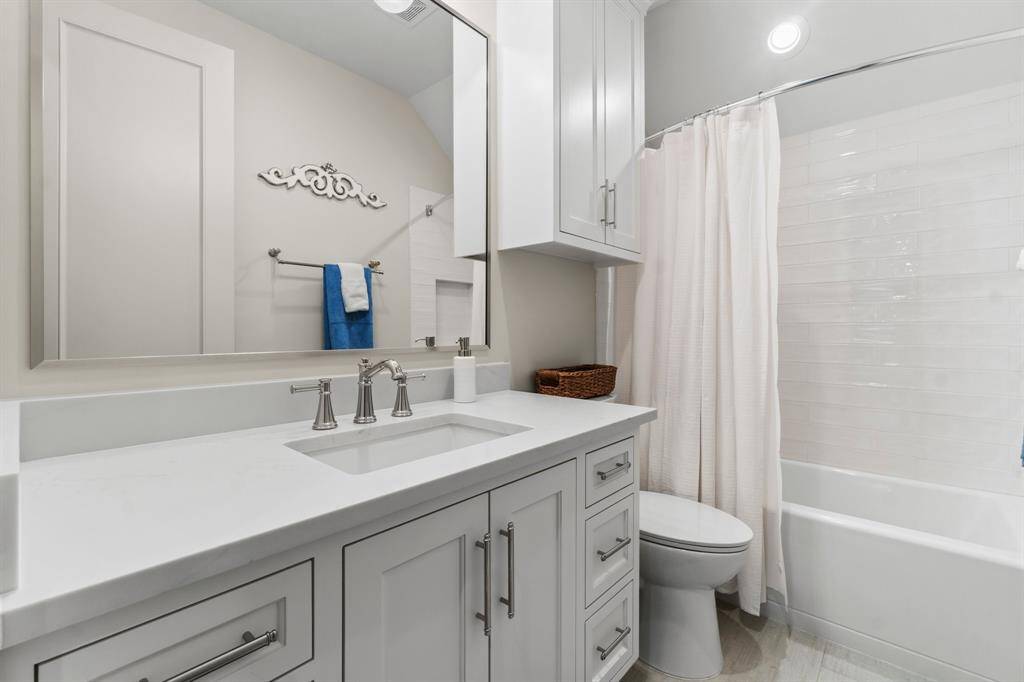 This bathroom features a modern design with a white vanity and sleek fixtures. It includes ample storage, a large mirror, and a combination shower-tub.