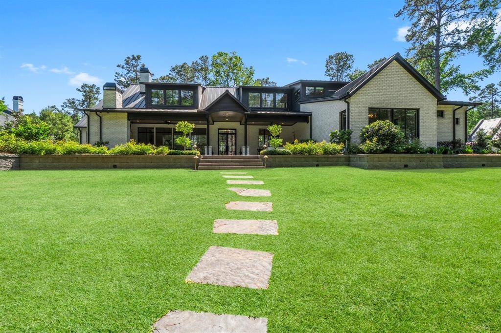 This modern home features a spacious, well-manicured lawn with a stone path leading to a welcoming patio. Surrounded by lush greenery, the house boasts a sleek, contemporary design with large windows, ideal for a serene living environment.