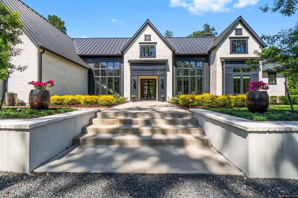 This property features a long, elegant driveway leading to a charming home surrounded by lush greenery and mature trees, offering privacy and a serene atmosphere. The entrance is framed by brick pillars, adding a touch of sophistication.
