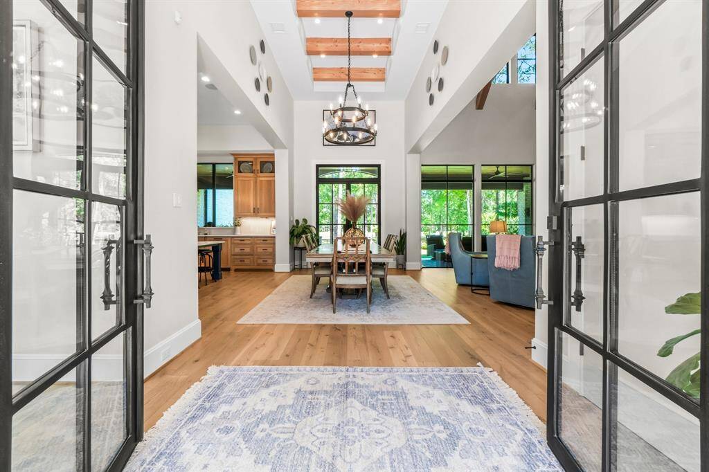 The entry reveals a bright and airy living space featuring expansive windows, rich wood flooring, and soaring ceilings with exposed beams.