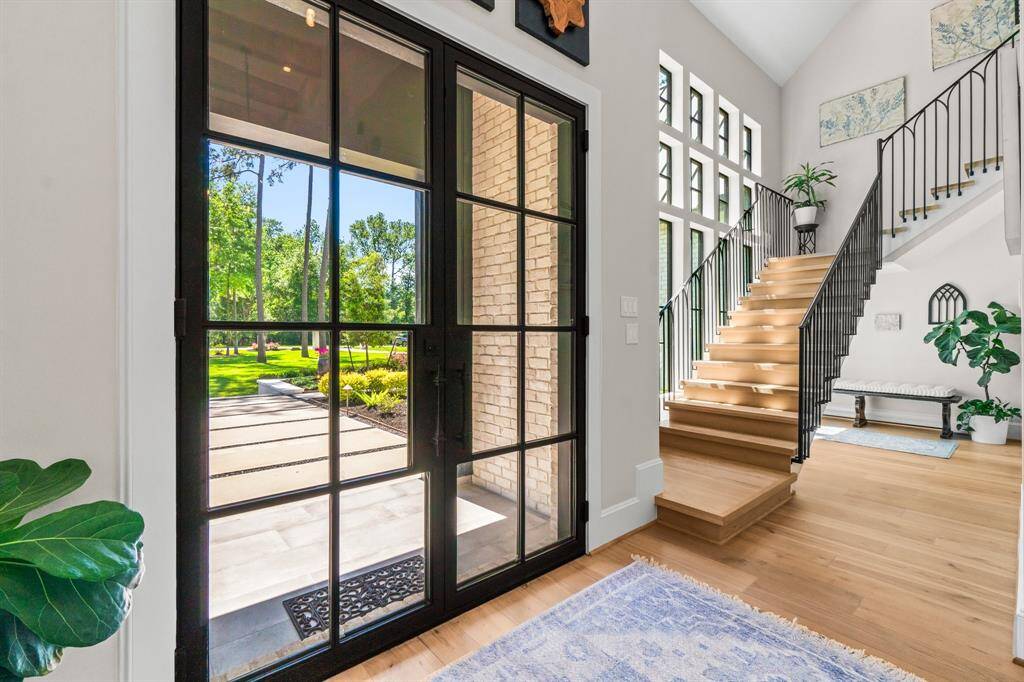This photo showcases a bright and inviting entryway featuring a large glass door with a view of the lush garden. The space includes a modern floating staircase with sleek railings, abundant natural light from tall windows, and warm wooden flooring, creating an elegant first impression.
