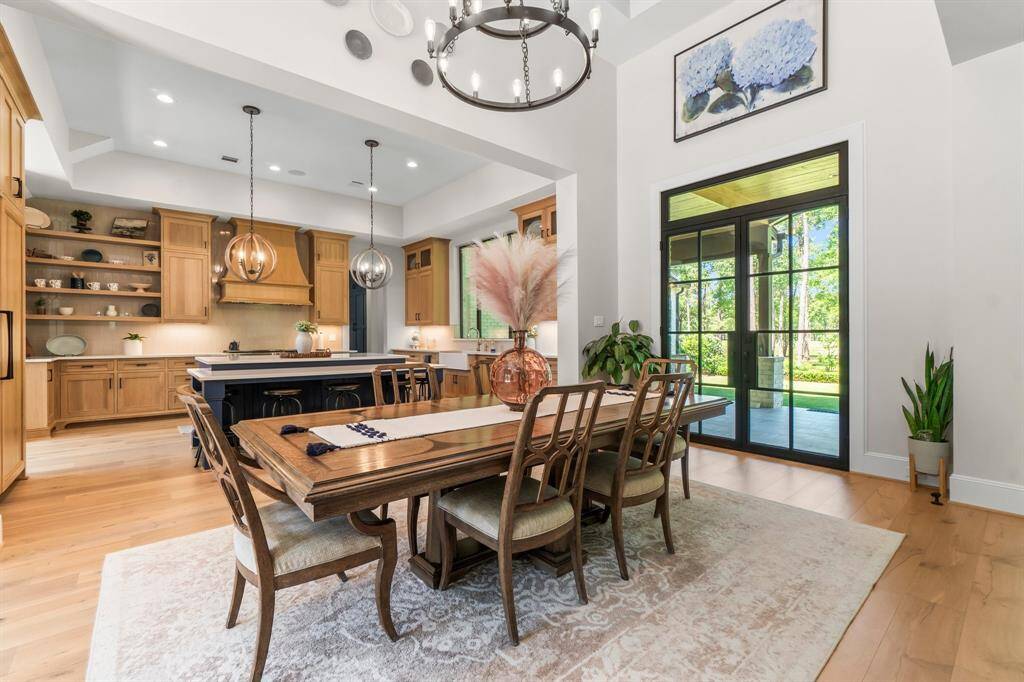This spacious, bright dining area features a chic light fixture, and opens to a modern kitchen with wood cabinetry and an island. Large glass doors enhance the room's airy feel.