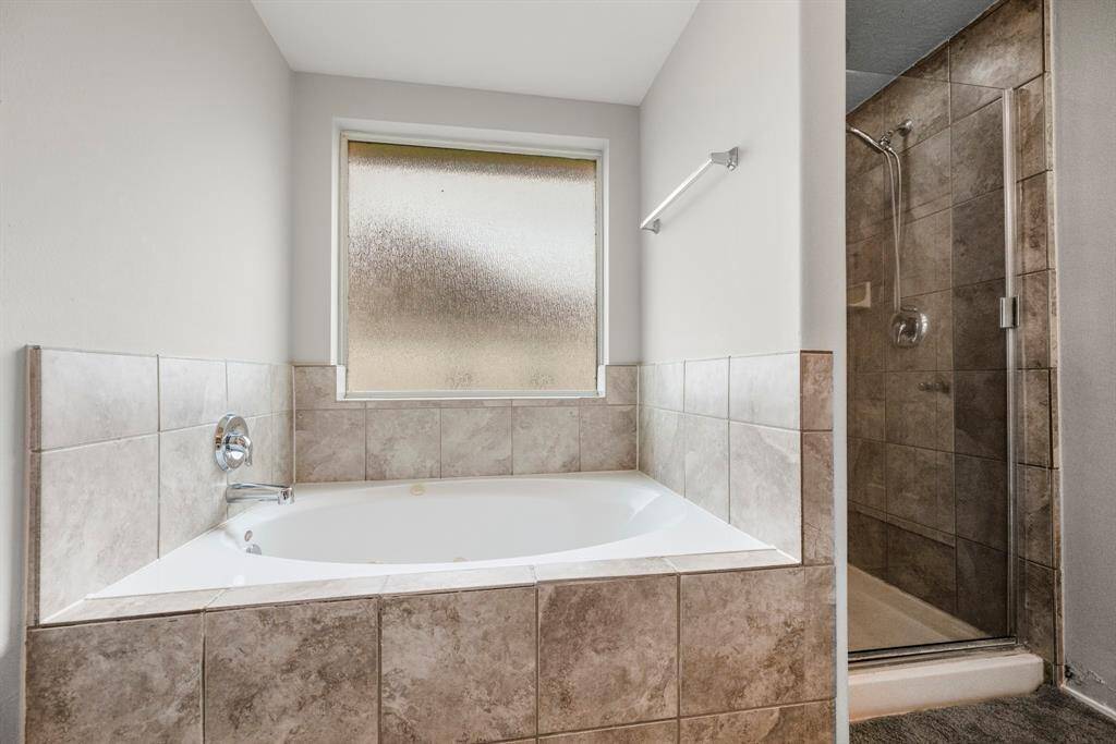 This primary bathroom includes a spacious shower with netural tile and glass surround. It's completed with a large garden tub allowing for a tranquil retreat.