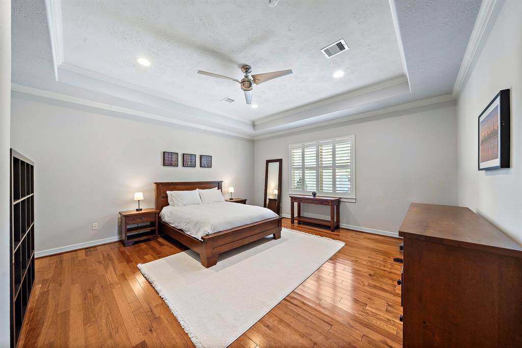 A serene escape, the spacious primary suite features tray ceilings, hardwood floors, and soft natural light filtering through plantation shutters. The tranquil ambiance invites rest, while its generous footprint easily accommodates a sitting area or workspace.
