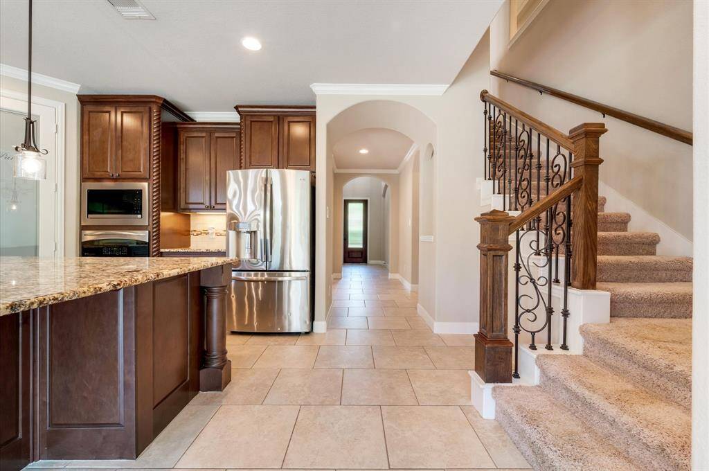 The open layout includes tile-floored hallway and an elegant staircase with wrought iron railings, leading to carpeted stairs.