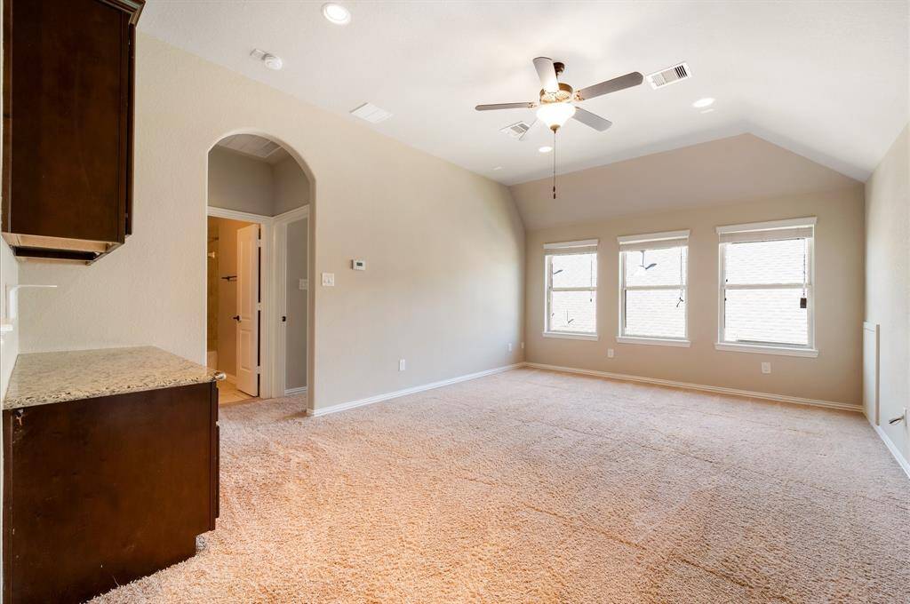 Upstairs spacious room with vaulted ceiling, featuring a ceiling fan and large windows for natural light. Carpeted flooring and an adjoining area with granite countertops offer functionality and comfort.