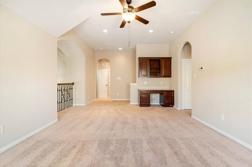 This spacious room includes a built-in desk with cabinets, perfect for a home office. Arched doorways and a decorative railing add elegant architectural details.