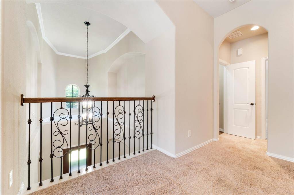 Elegant wrought iron railing overlooking the two-story space. An arched doorway leads to other rooms, and a stylish hanging light fixture adds a touch of sophistication.