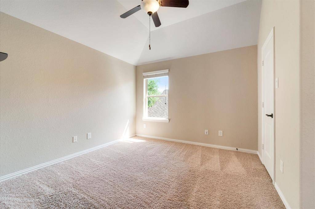 This other secondary  bedroom is a bright, carpeted with neutral walls, a ceiling fan, and a window providing natural light. The room has a vaulted ceiling and a door on the right.