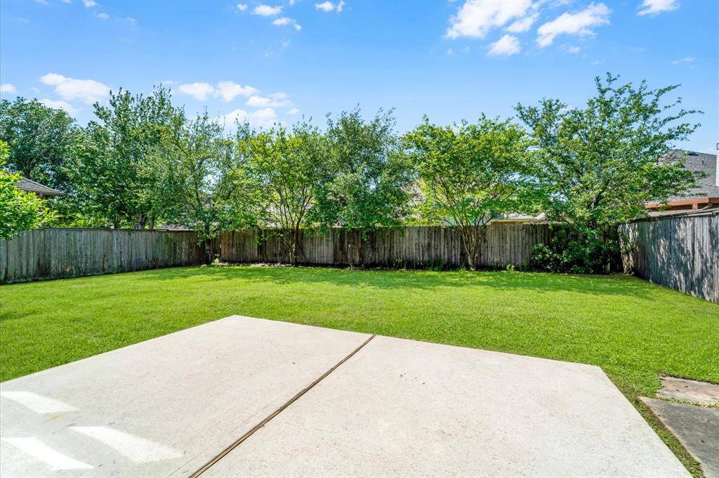 Spacious backyard with a large grassy area, bordered by a wooden fence and mature trees for added privacy. Ideal for outdoor activities and relaxation or maybe build your own pool.