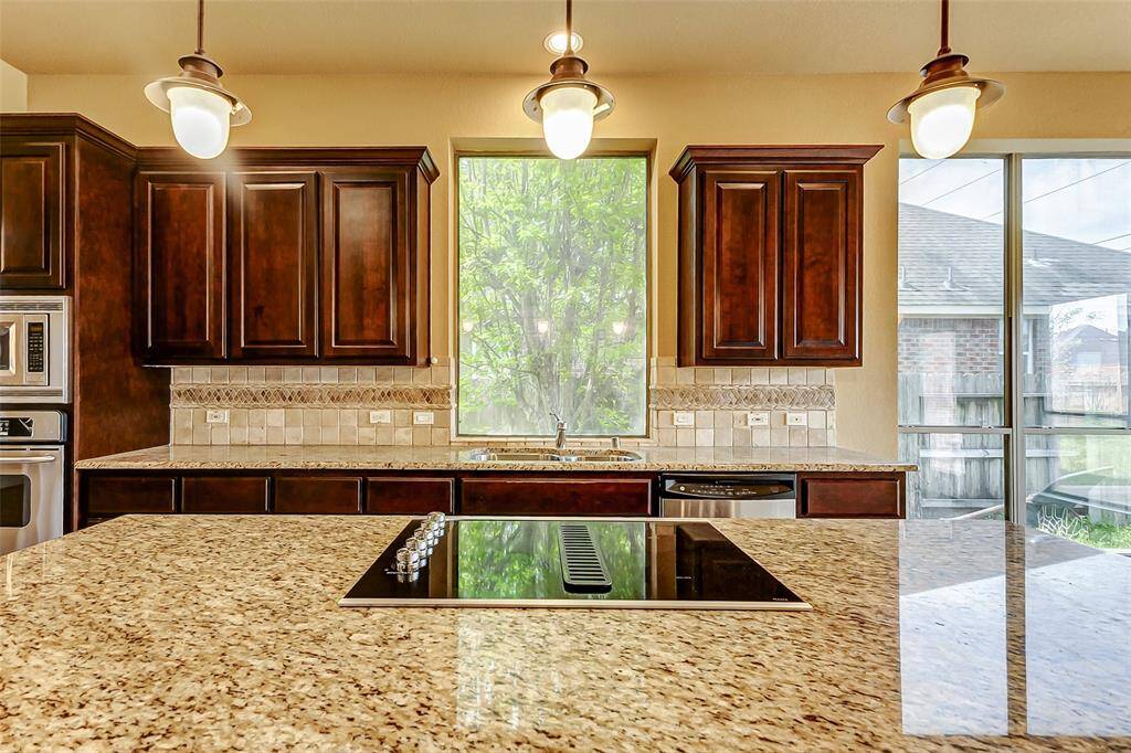 This kitchen features elegant dark wood cabinetry, granite countertops, and a modern cooktop on the island.
