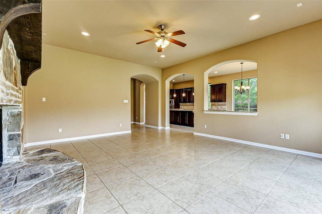 Spacious living area with tiled floors, a stone fireplace, and a ceiling fan.