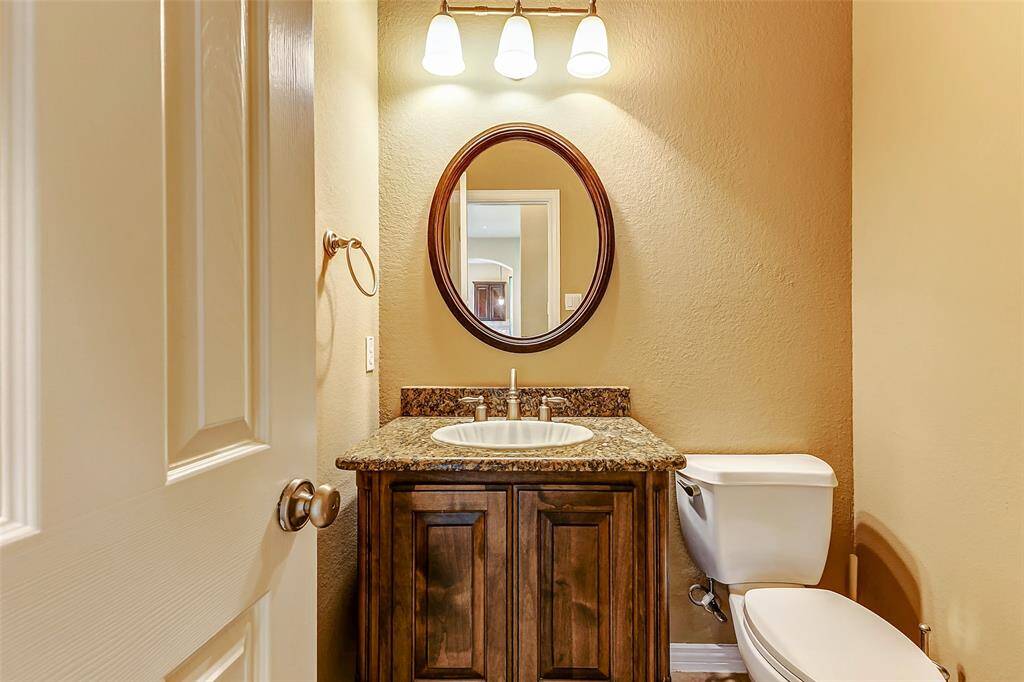 Elegant half bath featuring a granite countertop, a sophisticated wood vanity, and a stylish oval mirror.