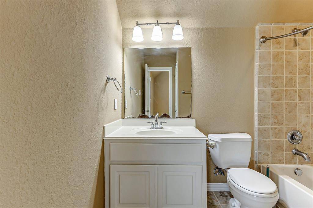Charming full bathroom featuring a sleek white vanity, expansive mirror, and elegant tiled shower-tub combo.