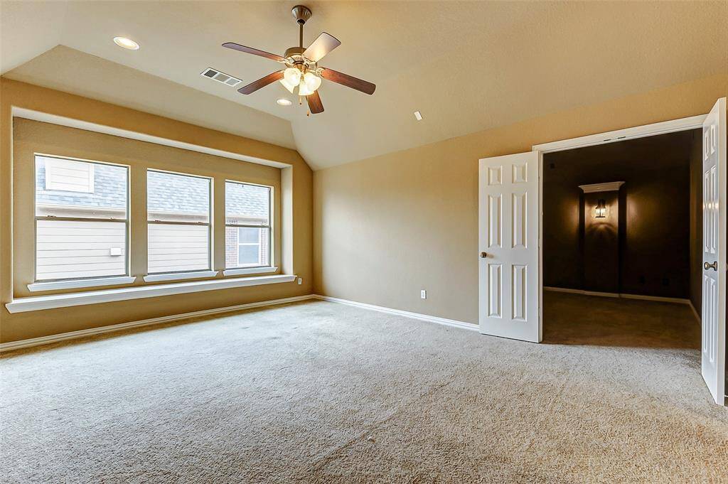 Bright, spacious room with neutral carpeting, vaulted ceiling, and ceiling fan.