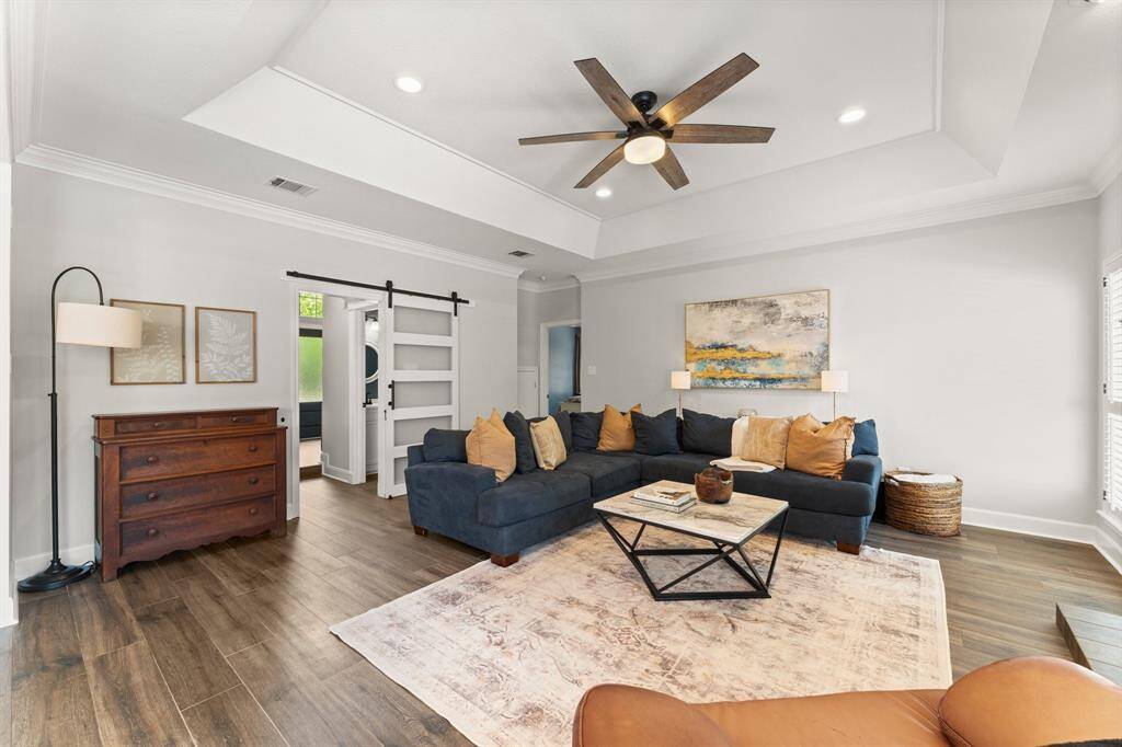 Family room with sliding barn door providing the option to close off for noise. Crown molding, tray ceiling, and shutters and wood look tile floors complete this room!