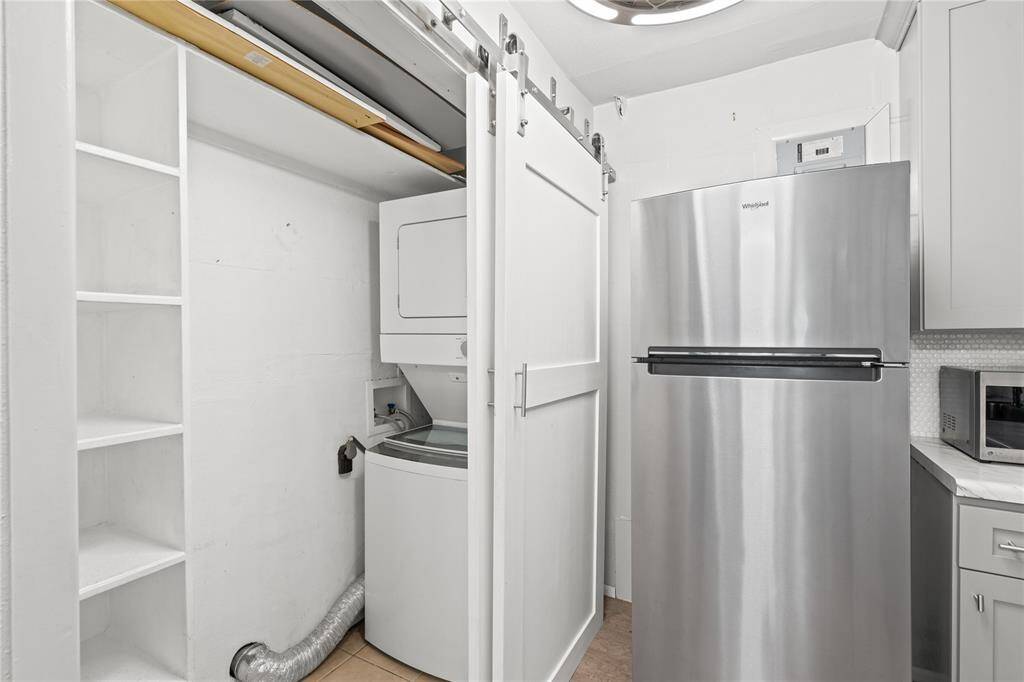 The refrigerator conveys with the home. To the left, hidden behind a barn door, you'll find pantry space and a stackable washer and dryer that also remain with the home.