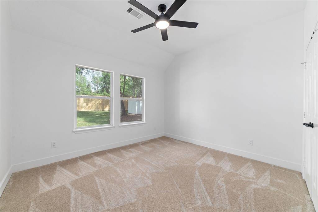 Second downstairs bedroom featuring plush carpet, soaring cathedral ceilings, and a modern ceiling fan.