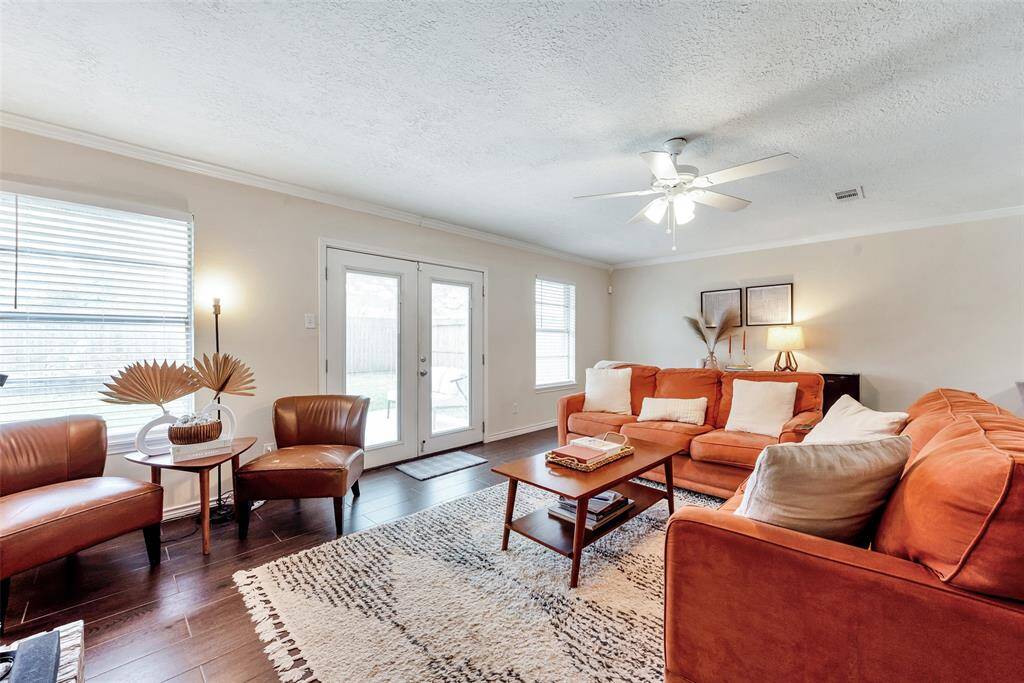 Large living room with wood look tile flooring, crown molding and lighted ceiling fan.