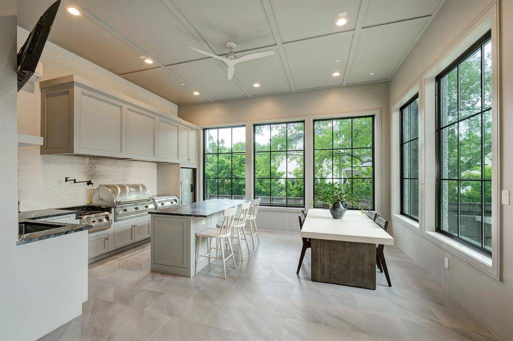 Auxiliary kitchen features premium commercial-grade appliances, including a Fire Magic Grill, Griddle, and Power Burner, complemented by a massive 96-inch commercial-grade ventilation system. The space includes custom cabinetry with beautiful leathered Crytos quartzite countertops, a utility sink, and a pot filler.