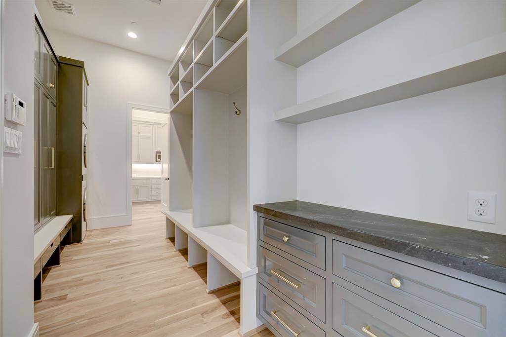 Stylish mudroom and utility space off the foyer includes custom cabinetry with elegant hardware, integrated washer/dryer, and a dedicated mail station with honed Diamond Black quartzite countertop. White oak flooring and designer finishes blend functionality with sophistication.