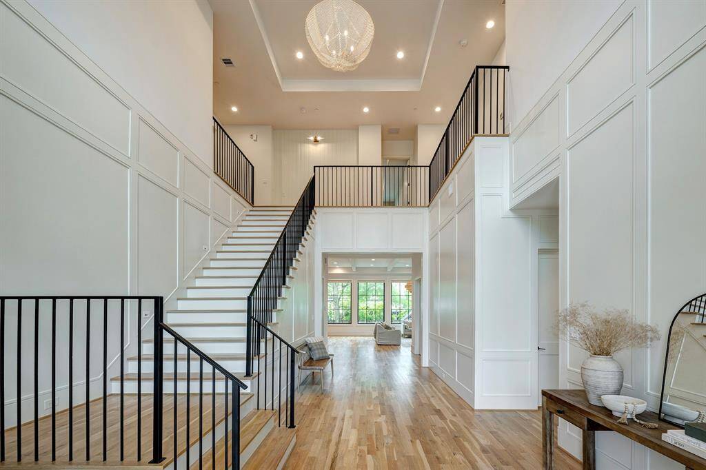 Step into a breathtaking two-story foyer that sets the tone for elegance and sophistication. The soaring 24-foot ceiling, custom iron railings, and elegant paneled walls create a striking architectural statement. Warm white oak hardwood floors flow throughout, complemented by a stunning chandelier that adds modern glamour. This expansive entryway creates a perfect first impression, seamlessly connecting the living area and upper-level landing.