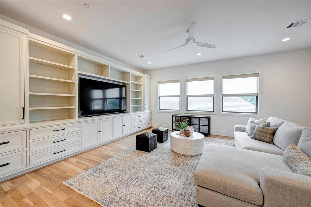 This light-filled game room seamlessly blends comfort and functionality with stylish custom design. White oak hardwood flooring adds warmth to the space, while an impressive 17-foot wall of custom inset cabinetry provides ample storage and display space. Matte black hardware creates a modern contrast against the soft, neutral palette. Three large windows equipped with custom window treatments from The Shade Store invite natural light and foster an inviting atmosphere—ideal for relaxing or entertaining.